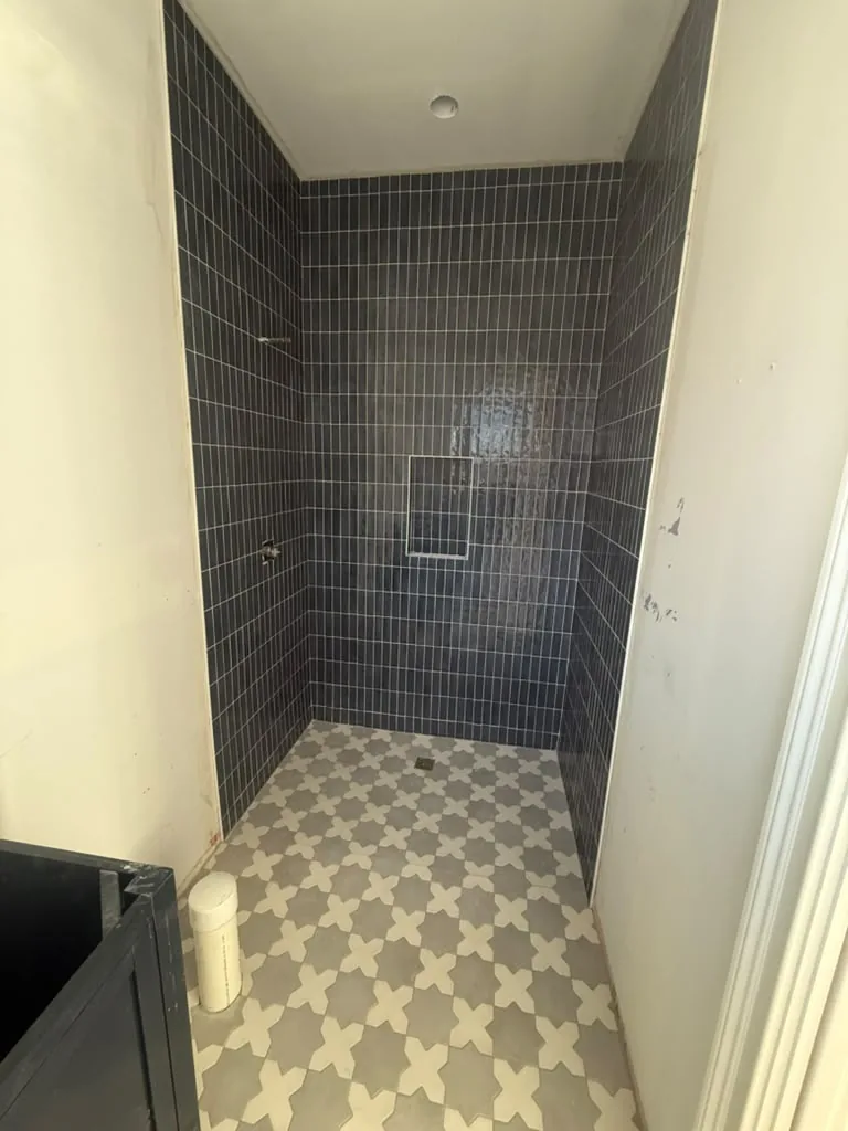 Shower with dark subway tile and patterned hex floor
