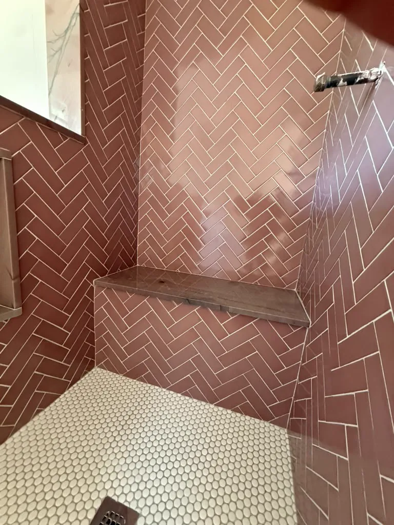 Herringbone shower with wood bench and white hexagon floor