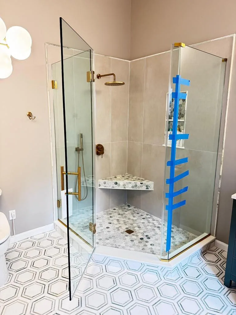 Corner glass enclosure with gold hardware over a hex tile floor