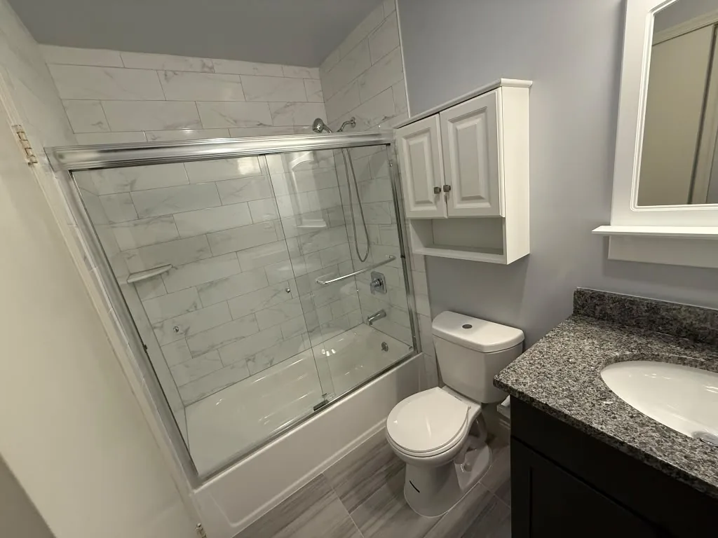 Custom glass shower enclosure with chrome hardware over a tiled tub