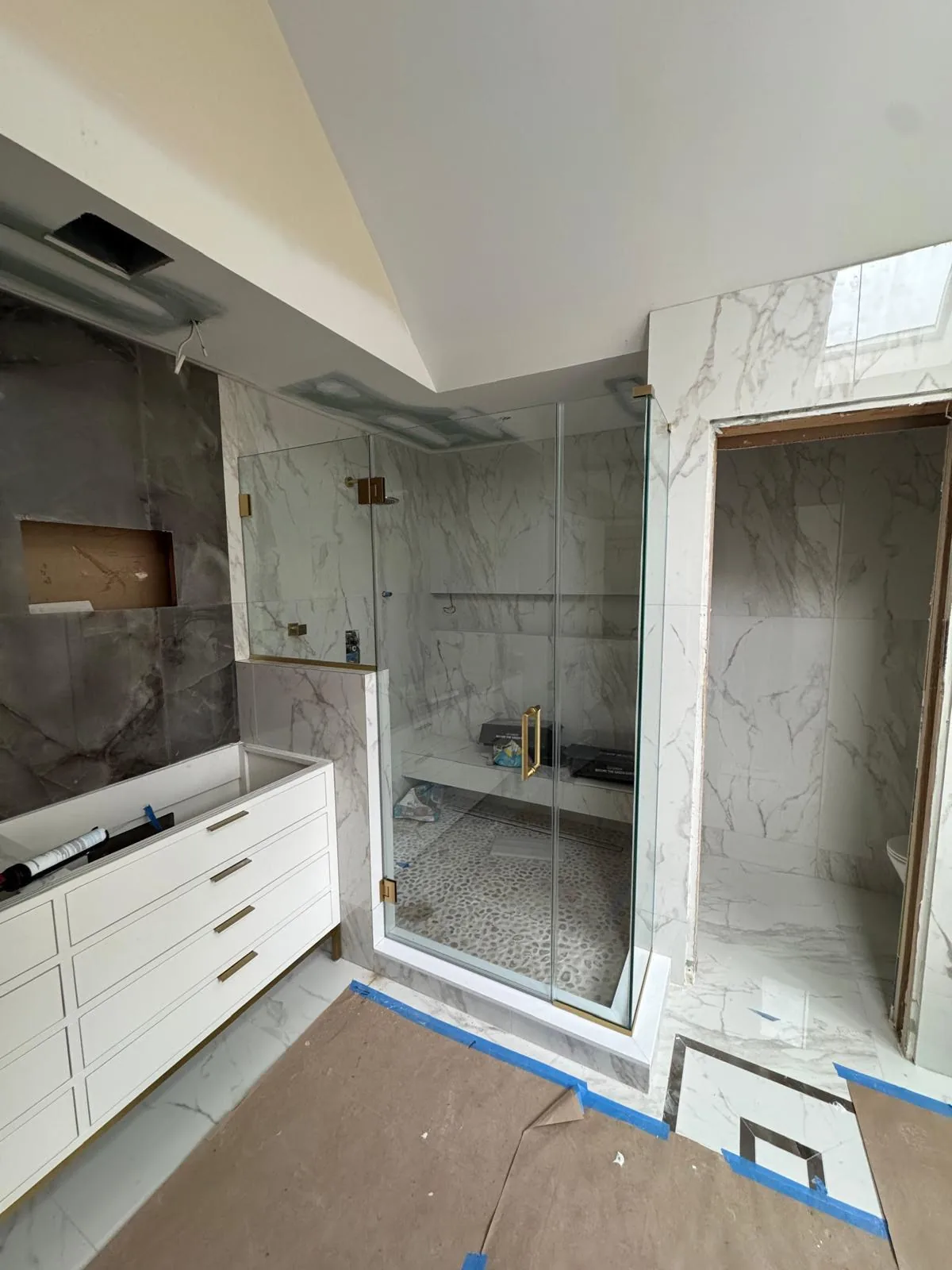 Frameless glass enclosure with gold hardware in a marble bathroom