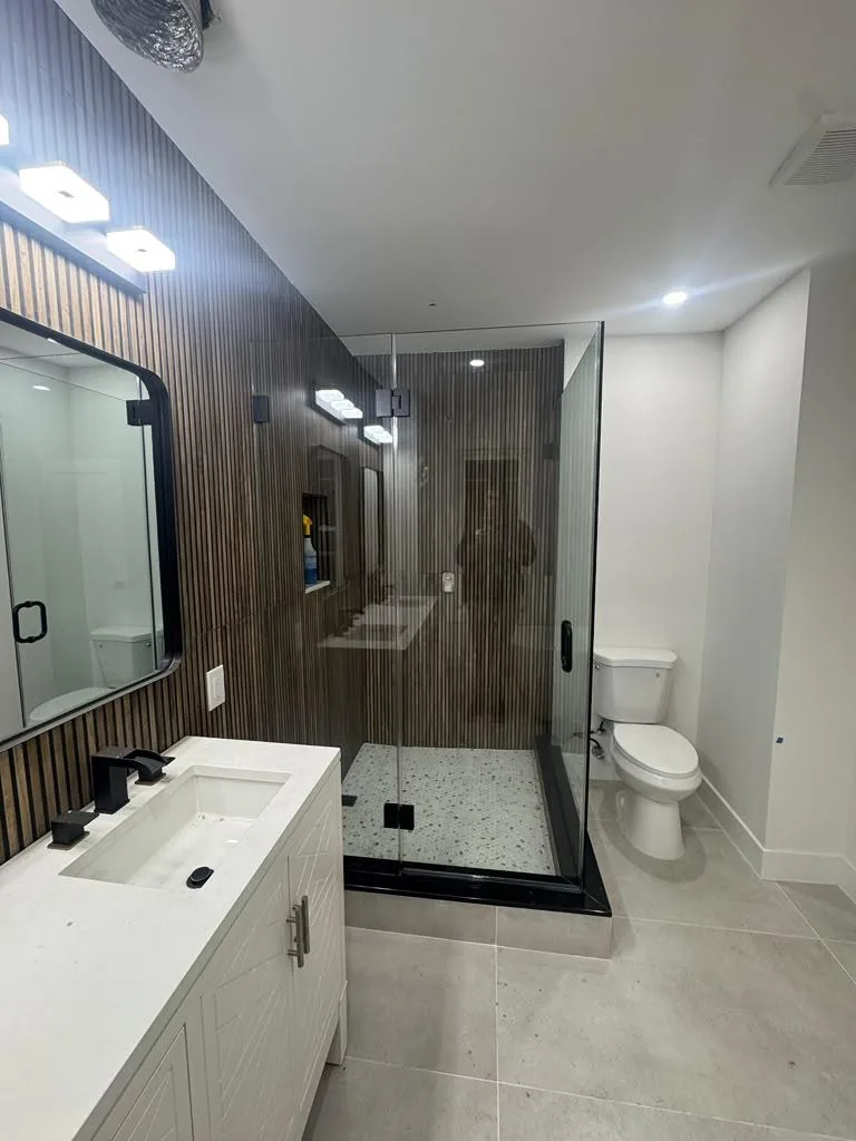 Glass shower with black hardware beside a slatted feature wall