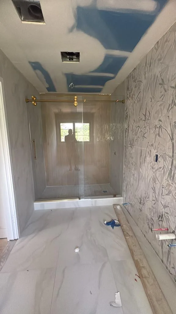 Sliding glass shower door with gold rail on a marble walk-in shower