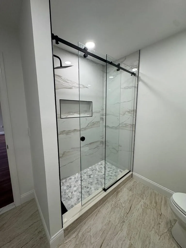 Sliding frameless glass door on a marble shower with pebble floor