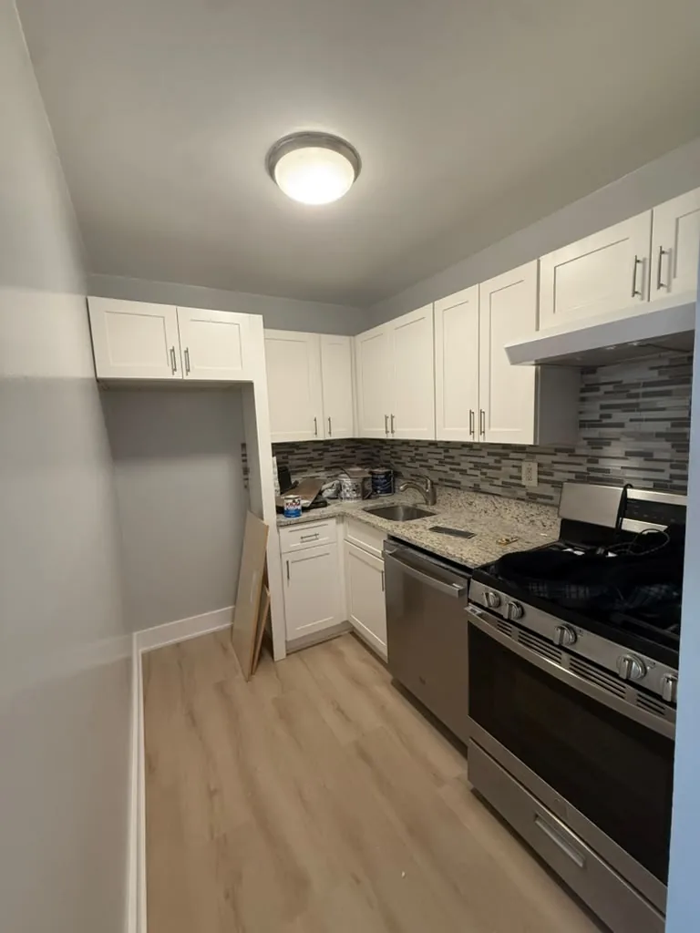 Renovated kitchen with white shaker cabinets, stone counters and tile backsplash