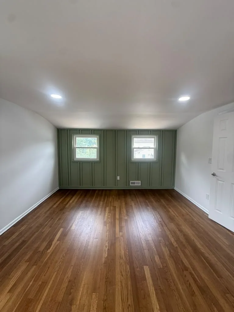 Living room with sage green accent wall and refinished hardwood floors