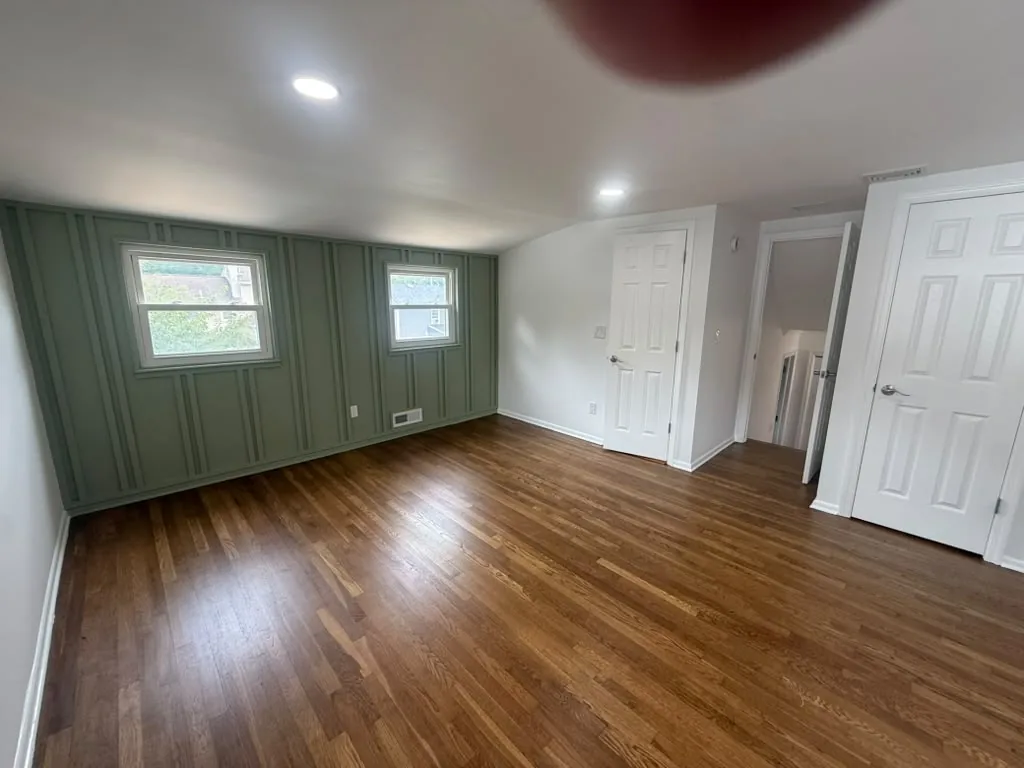 Room with green accent wall, white trim and hardwood floors