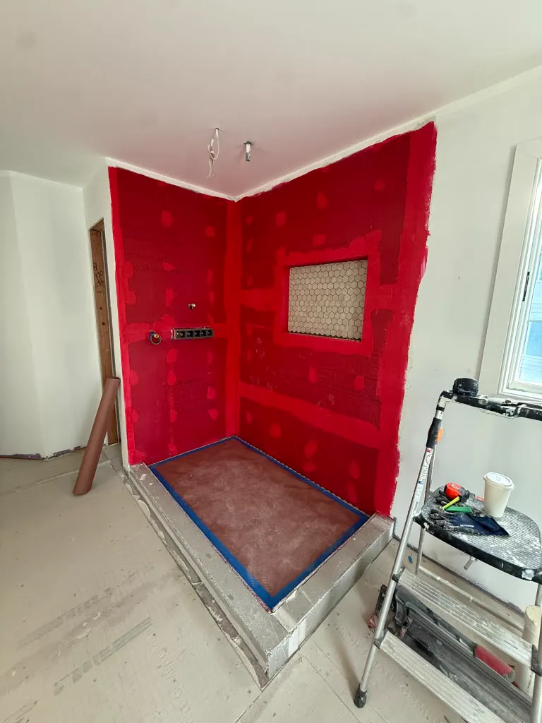 Full shower coated in red waterproofing membrane with niche and curb, ready for tile